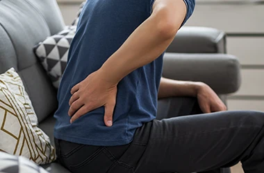 Person sitting in a chair with their hand on their lower back.