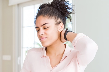 Woman with a pained expression holding her neck.